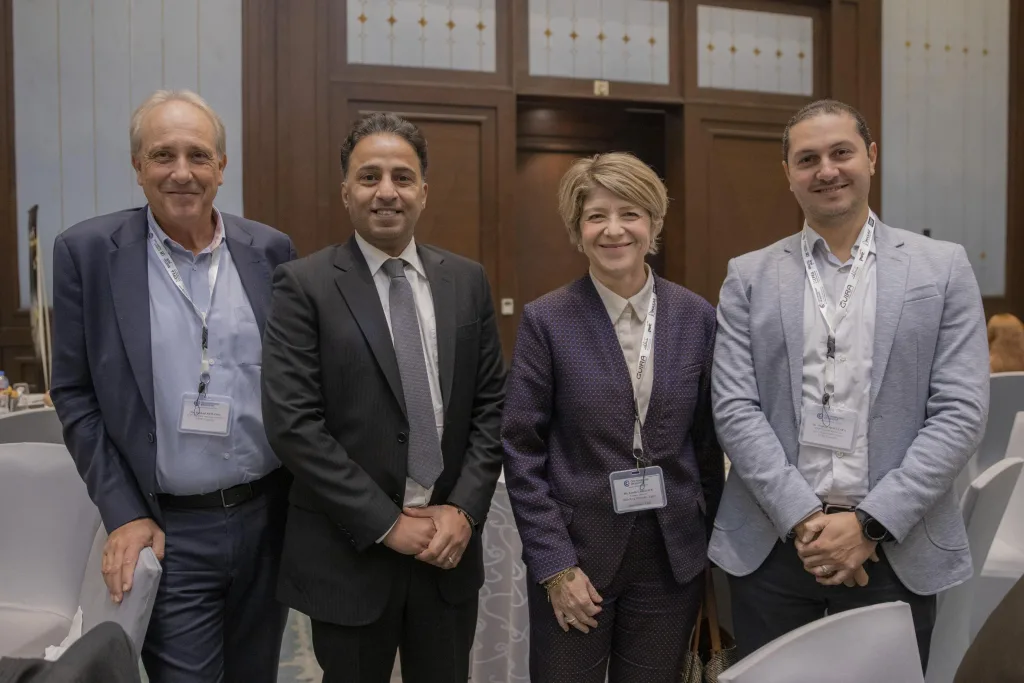 A formal group photo of three ECPC men in business attire standing with the female CFO of Heidelberg Materials at a business forum in a conference hall.