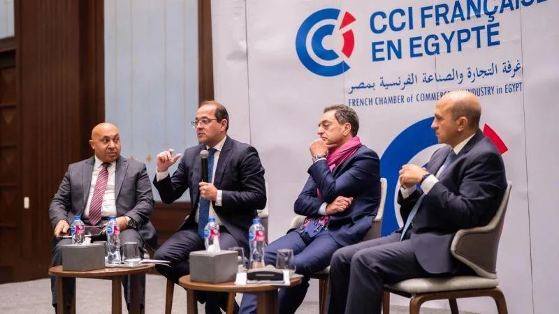 Egyptian Minister of Finance Ahmed Kouchouk speaking at a microphone during a CCIFE panel discussion in Egypt, seated with three other delegates in front of a French Chamber of Commerce backdrop.